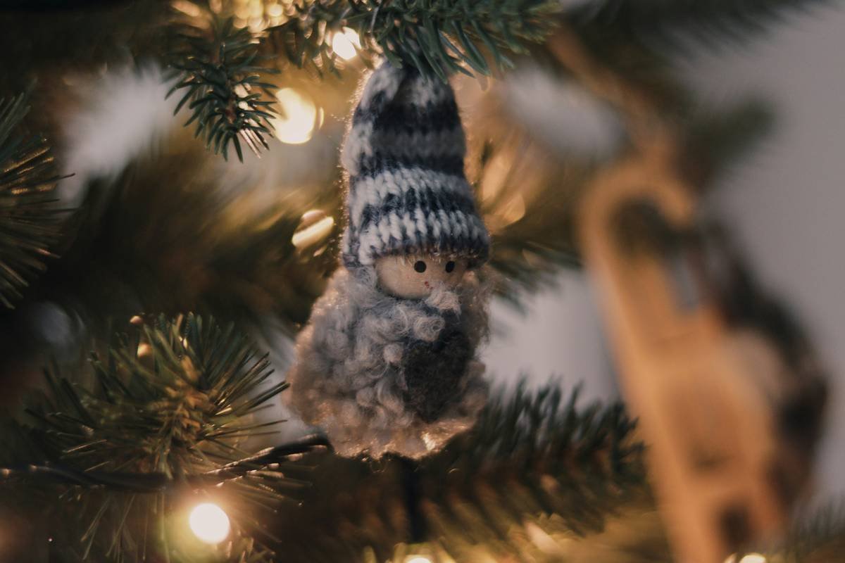 Close-up of a beaded snowflake hook suspending a vintage glass ornament on a pine Christmas tree branch
