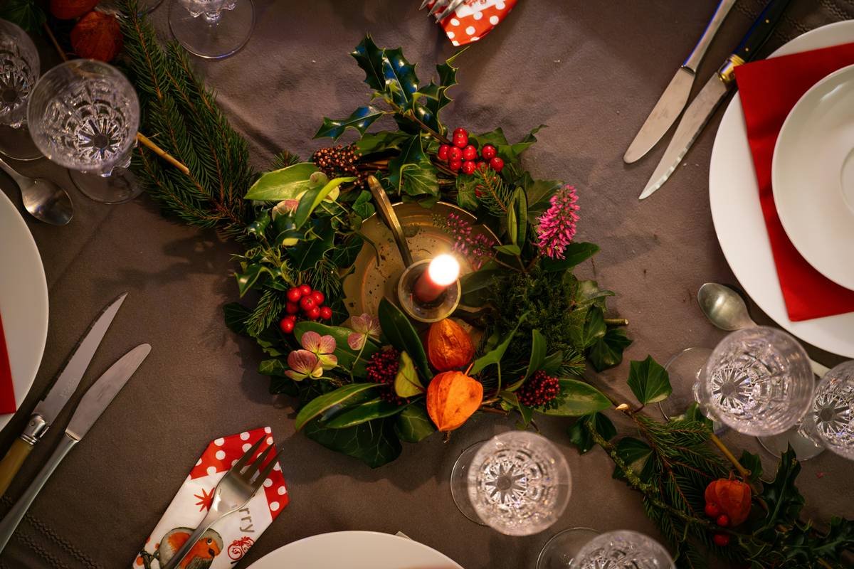 candle ring faux greenery arranged around a cream pillar candle on a wooden table, showing realistic eucalyptus stems and dusty miller accents